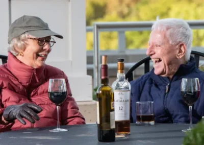 Two elderly individuals sharing a laugh at a table with wine glasses and a bottle of macallan 12.