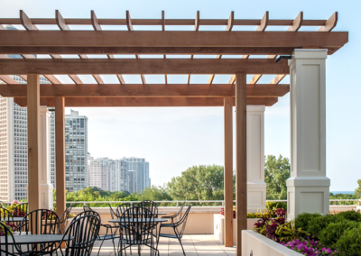 Wooden pergola and outdoor seating area on a rooftop garden with city skyline in the background.