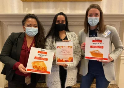 Three women wearing masks and holding pie boxes at an event.