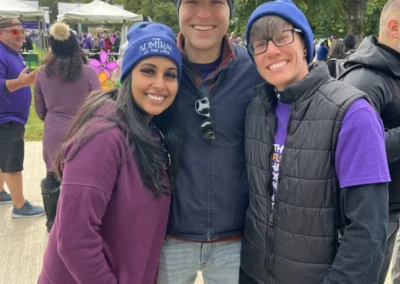 Three people smiling at an outdoor event, with two wearing purple garments and one in a navy jacket.