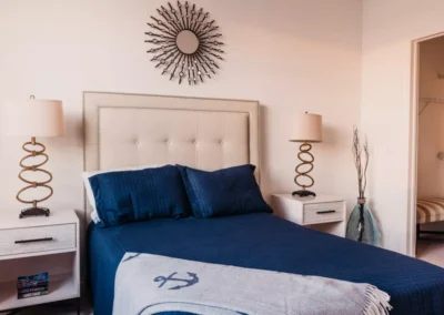 A stylish bedroom featuring a neatly made bed with dark blue bedding, two side tables with lamps, and a decorative mirror above the bed.